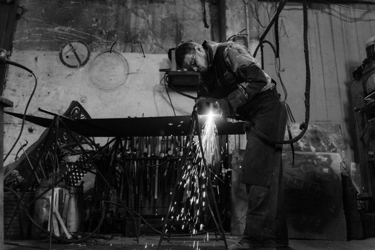 Black and white image of a welder working with sparks flying in an industrial setting.